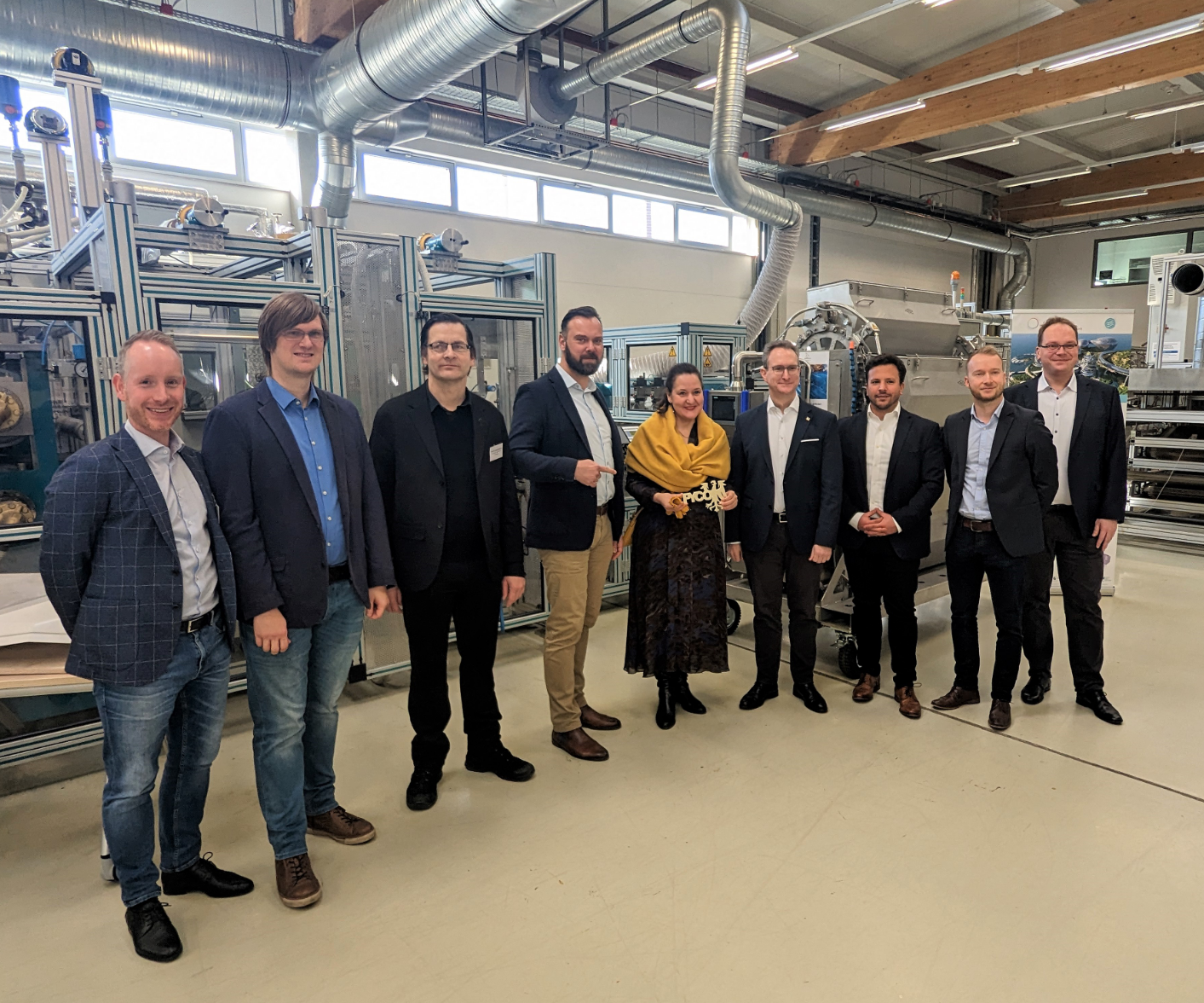 nine people stand in a row in a factory hall